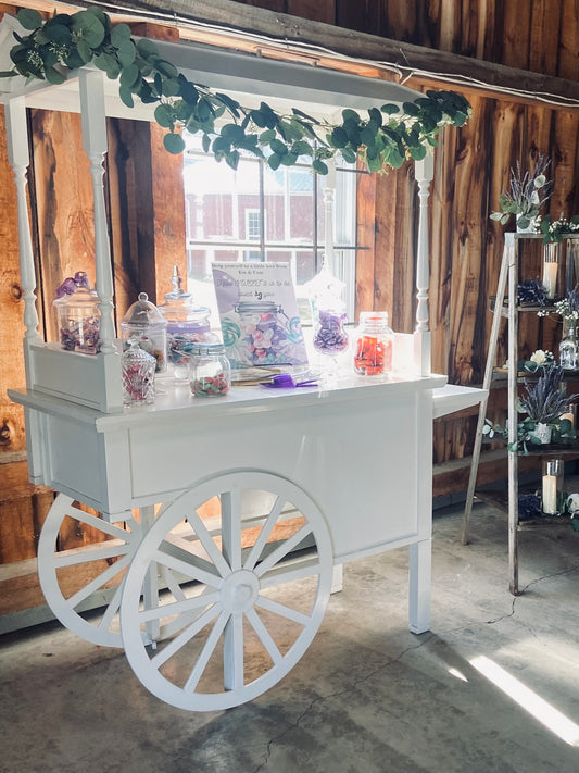 candy cart decorated in a barn setting with eucaptus garland on top